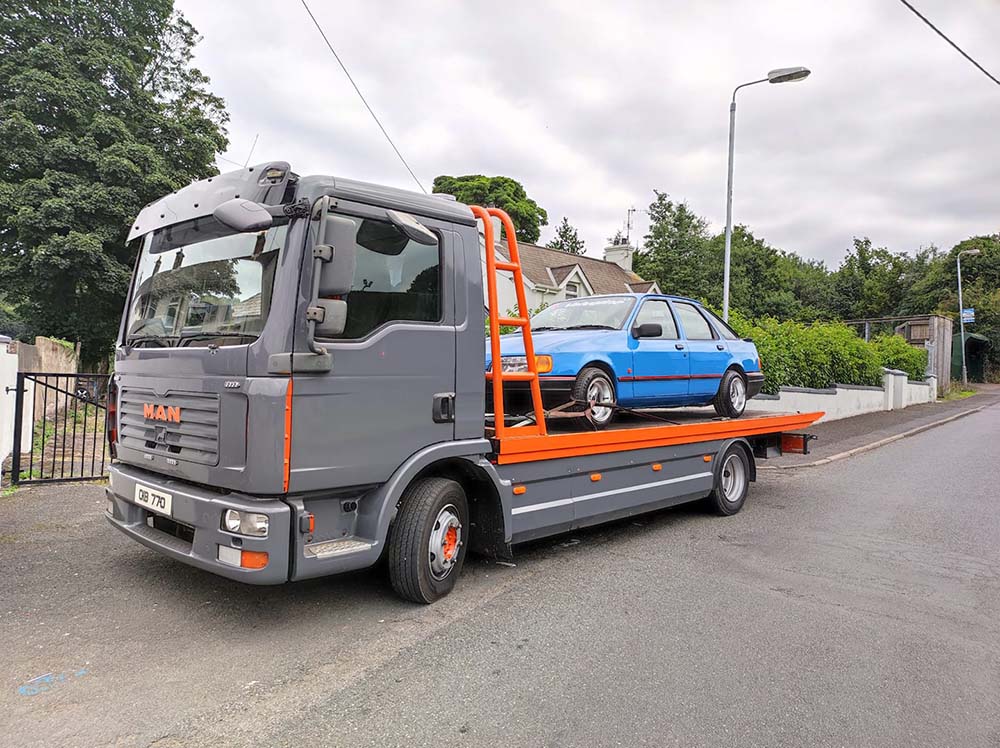orange and grey recovery truck towing blue car